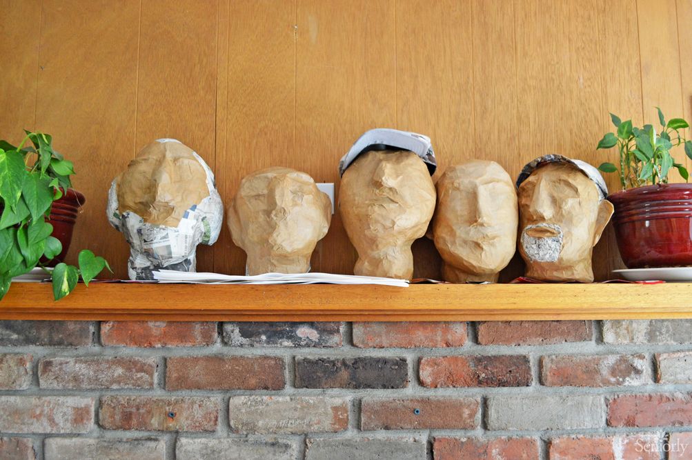 A display of plaster head sculptures on a wooden shelf against a brick wall.