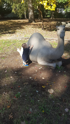 A curious child exploring the back of a life-sized elephant statue in a park.