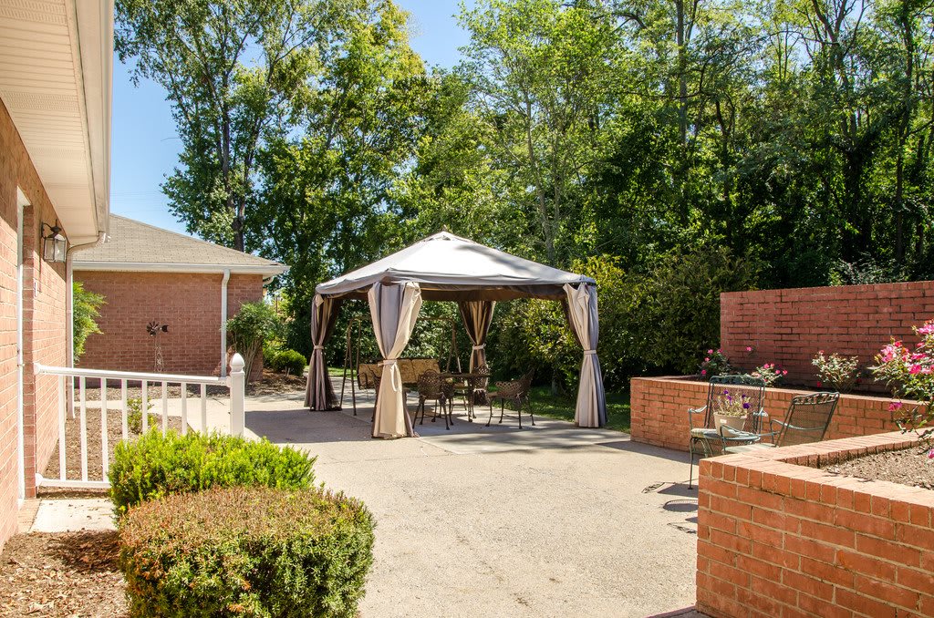 A sunny outdoor patio with a gazebo and surrounding greenery.