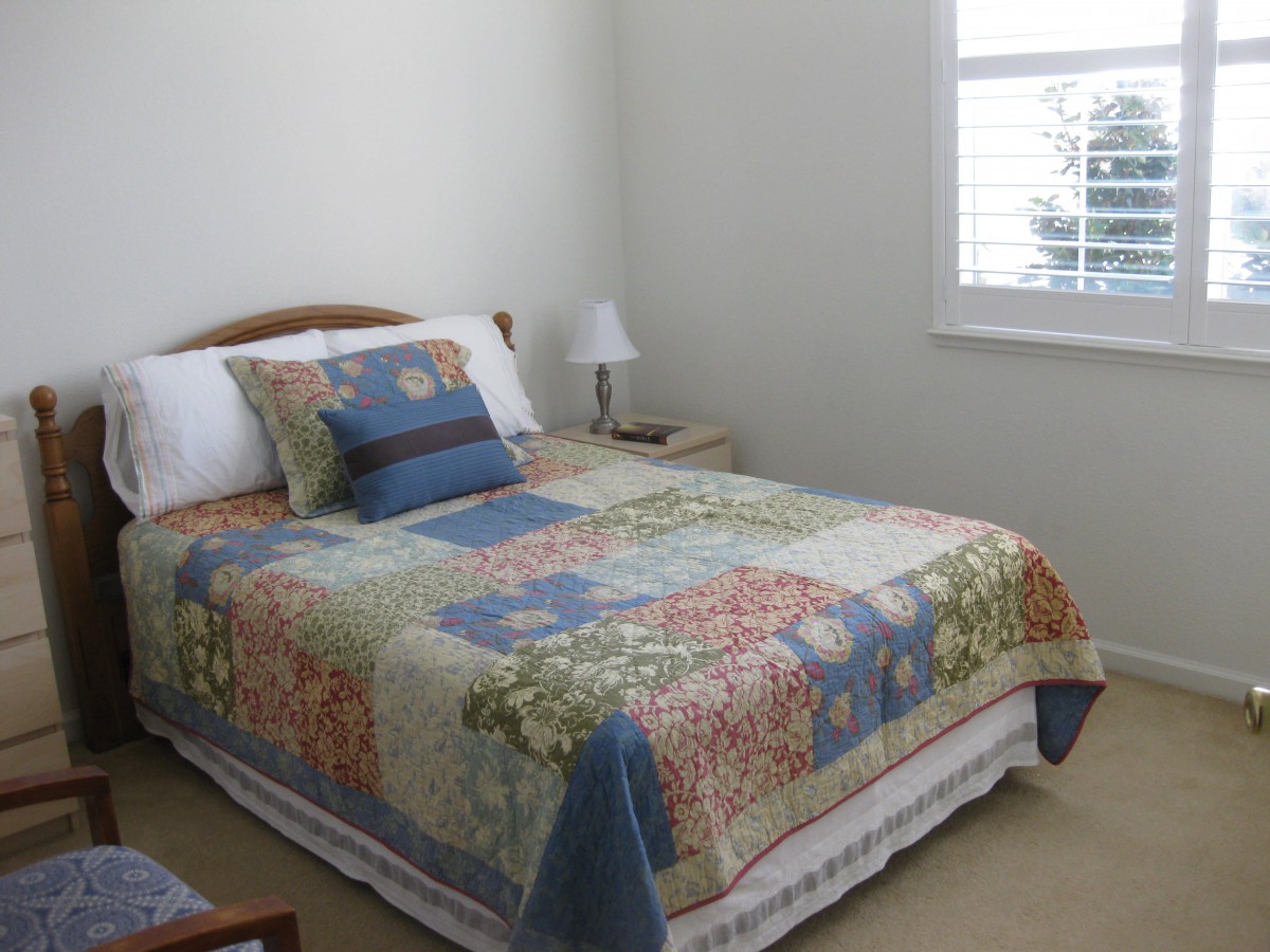 A cozy bedroom with a colorful quilt on the bed and a lamp on the side table.