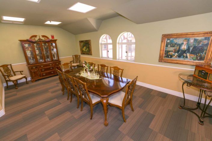 A well-appointed dining room featuring a large wooden table set with chairs, surrounded by decorative artwork and a display cabinet.