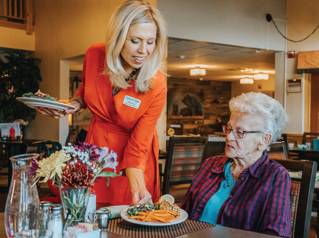 A staff member assists a senior woman with her meal at a restaurant.