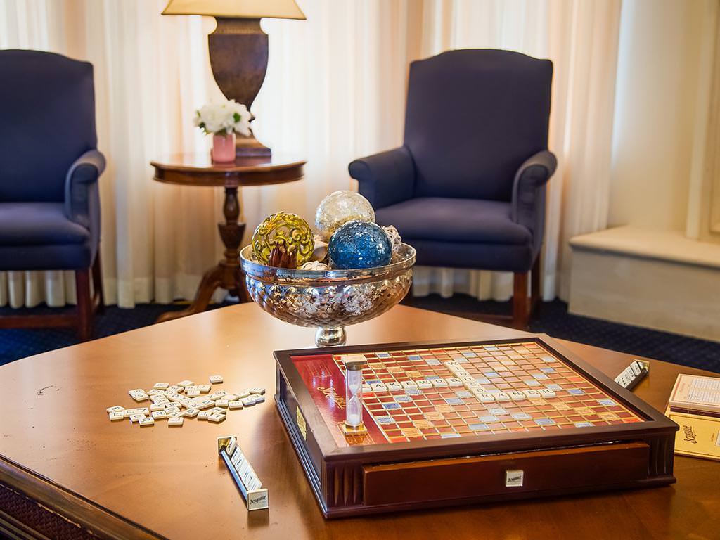 A cozy living room with a Scrabble game on the coffee table and comfortable blue chairs in the background.