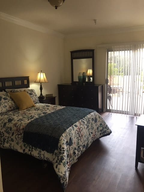 A cozy bedroom with a bed, dresser, and a window with curtains letting in natural light.