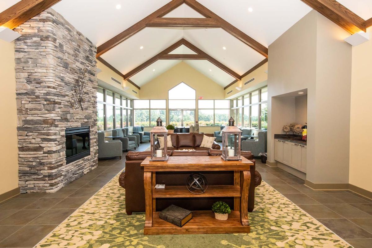 A spacious living room featuring a vaulted ceiling with wood beams, a stone fireplace, and modern furnishings, illuminated by natural light from large windows.