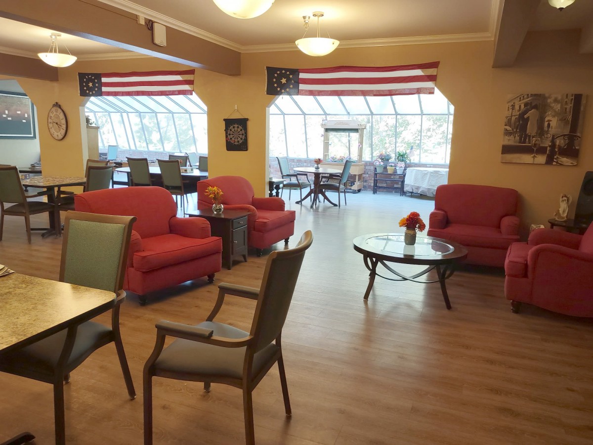 A cozy seating area with red sofas, chairs, and tables under a large window adorned with flags.