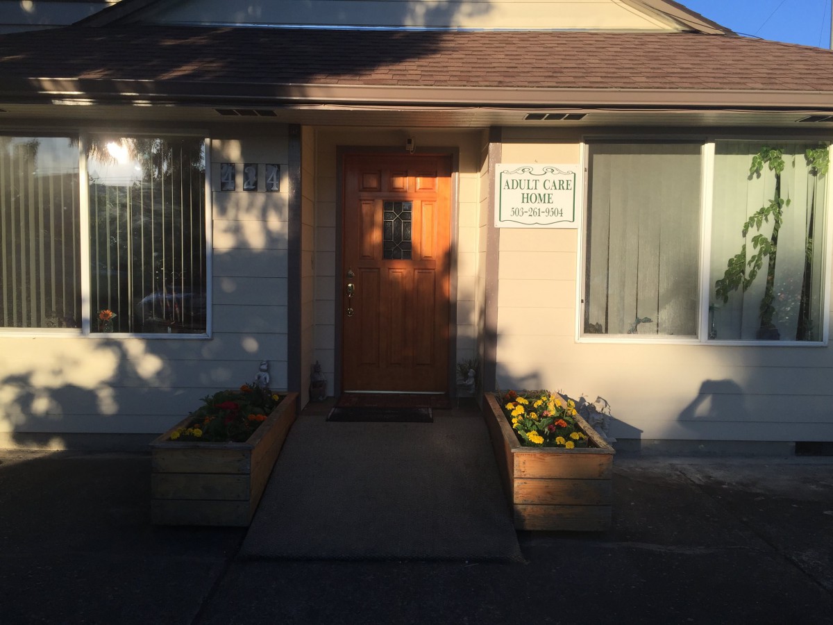 A house entrance with a wooden door and planters, illuminated by sunlight.