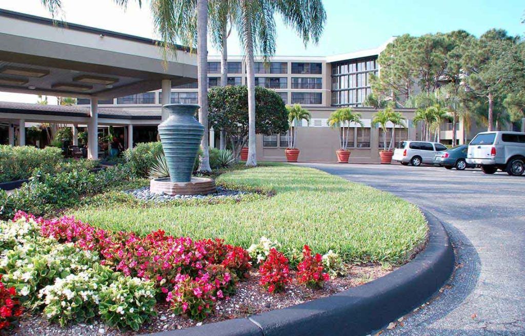 The exterior of a hotel featuring landscaped gardens and palm trees at the entrance.