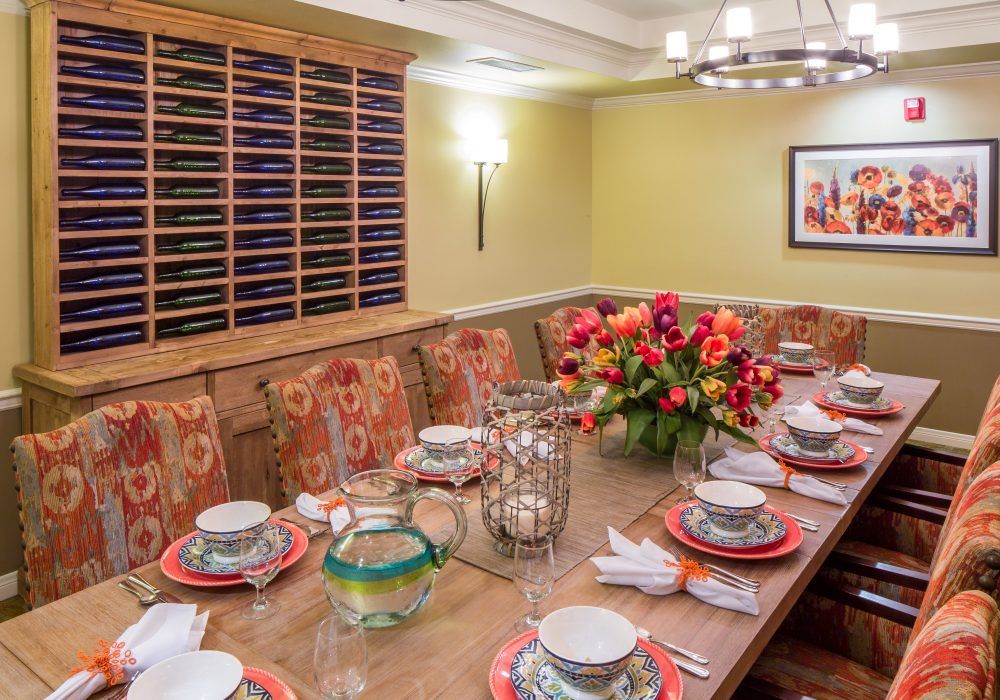 An elegantly set dining table with floral arrangements and upholstered chairs in a warmly lit room.