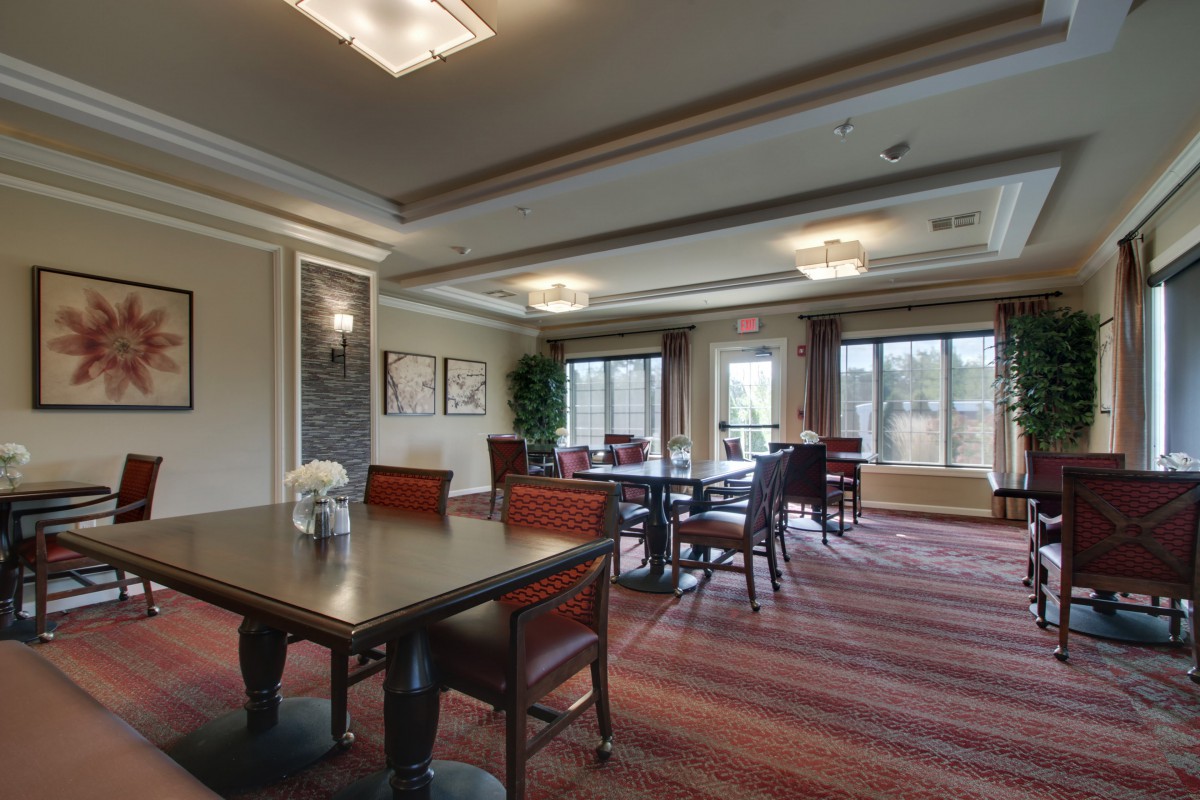 A well-lit conference room featuring multiple tables and chairs, with large windows providing natural light.