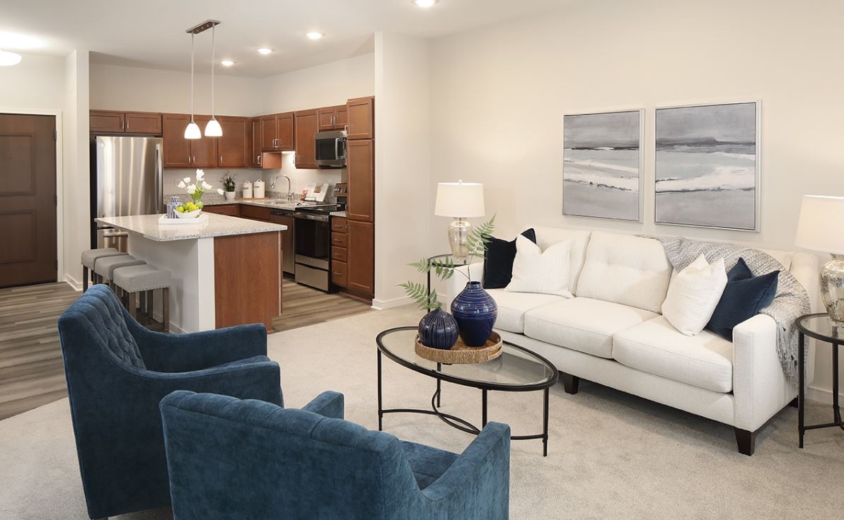 A modern open-layout living room with a connected kitchen, featuring a white sofa, blue chairs, and decorative elements.