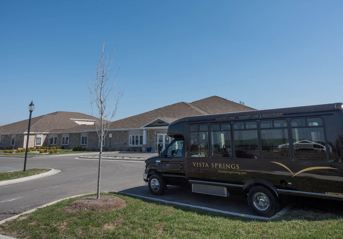 A small bus is parked in front of a large building on a clear day.