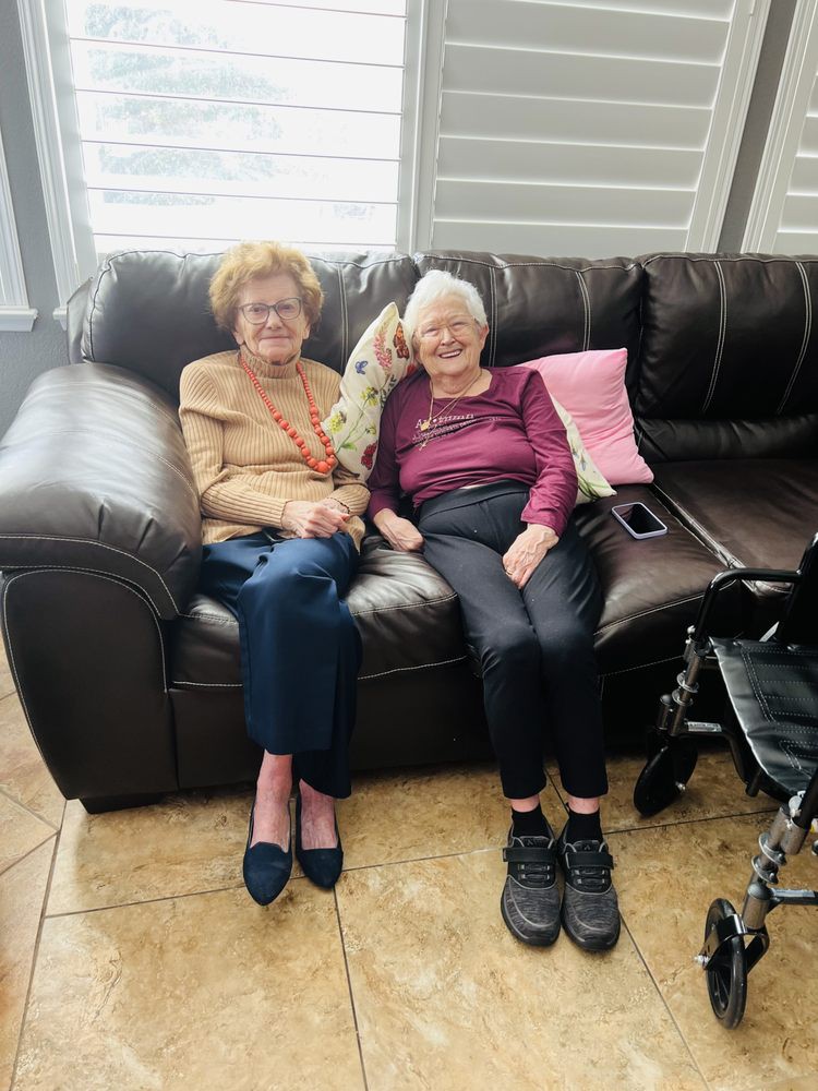 Two elderly women sitting together on a couch, smiling and enjoying each other's company.