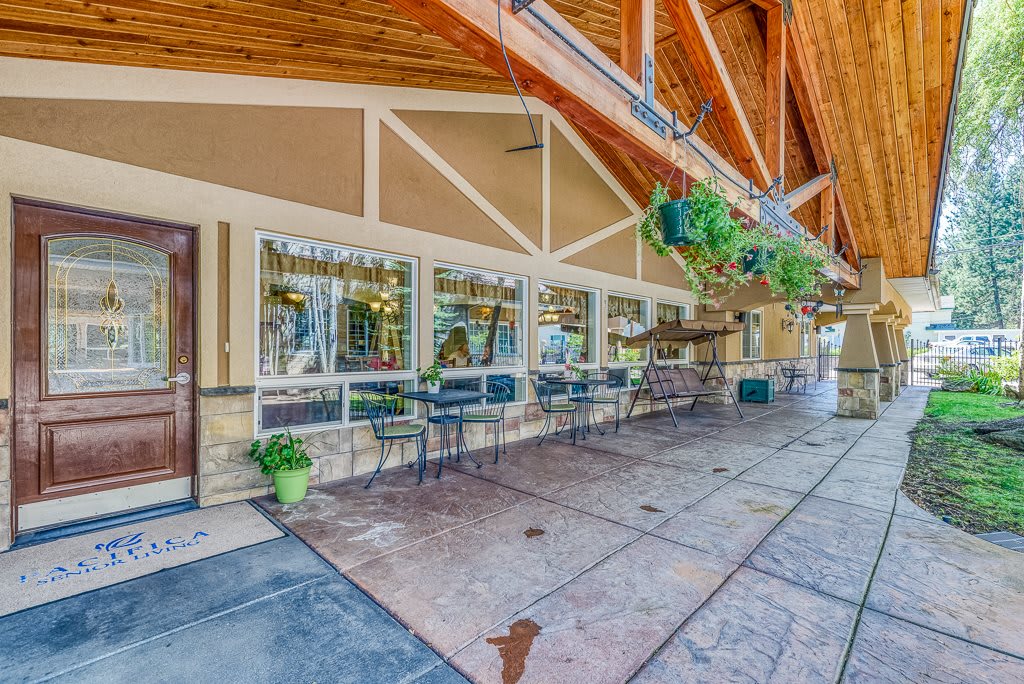 An inviting restaurant patio with outdoor seating under a wooden canopy, adorned with hanging plants.