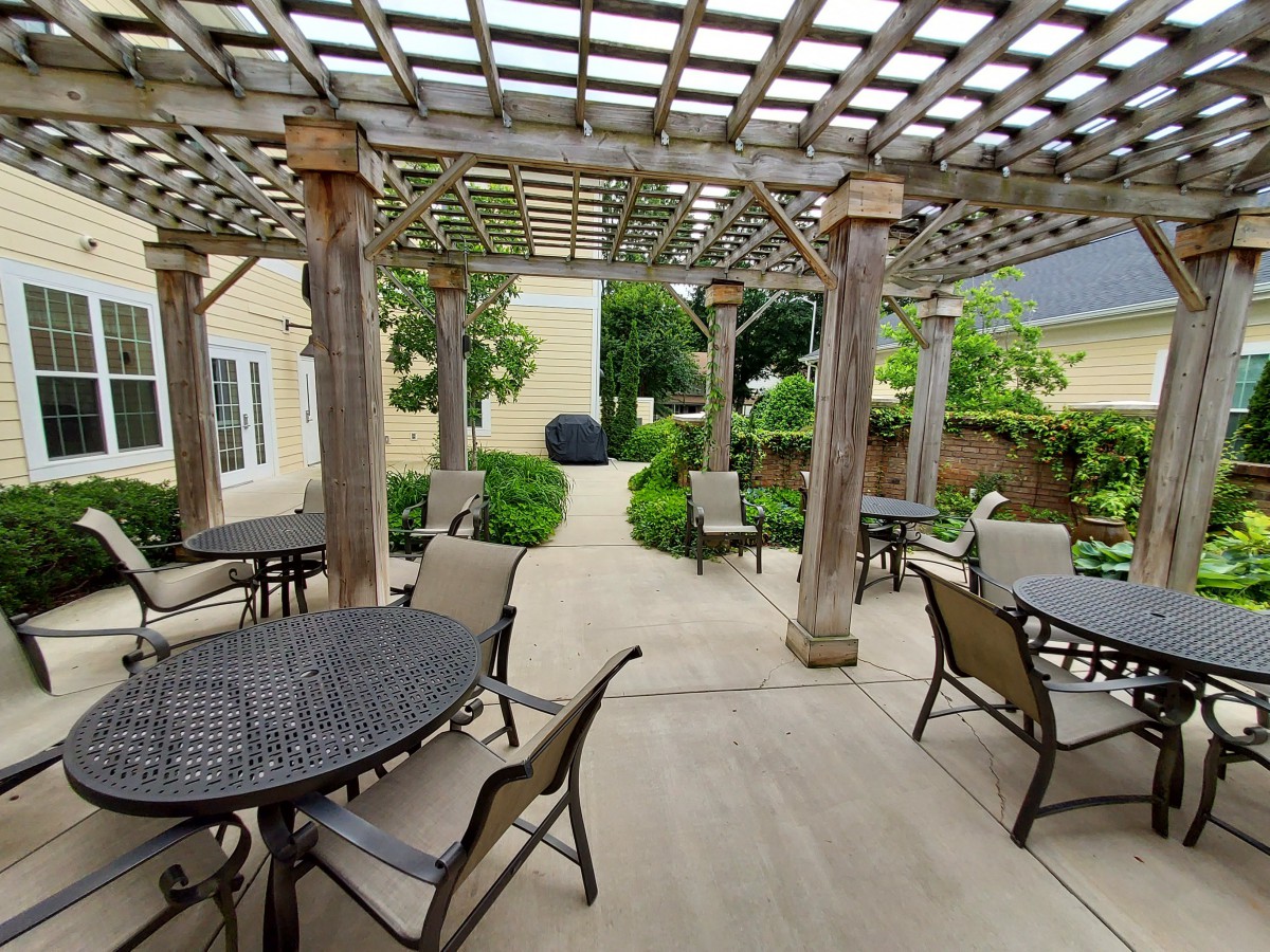 A beautiful outdoor patio area with a pergola, tables, and chairs, surrounded by lush garden landscaping.