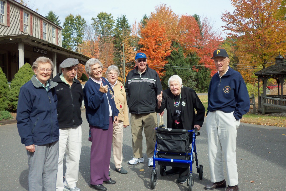 A group of older adults enjoying a beautiful autumn day outdoors with colorful foliage in the background.