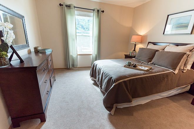 A cozy bedroom with a neatly made bed, a lamp on the nightstand, and a dresser near the window.