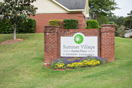 A brick sign for Summer Village, surrounded by landscaping and flowers.