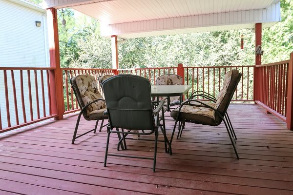 A cozy outdoor patio with a table and cushioned chairs on a covered deck.
