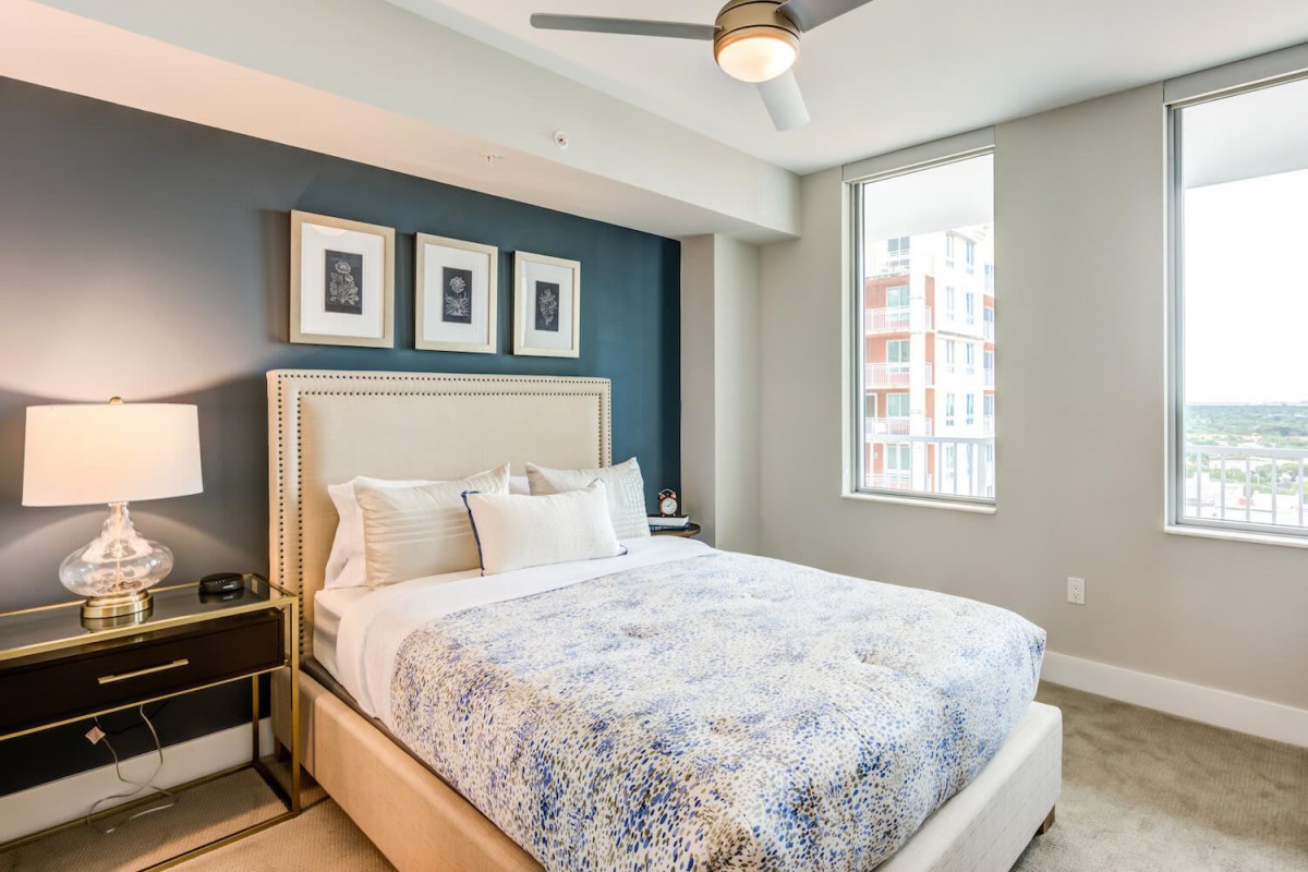 A modern bedroom with stylish decor, featuring a comfortable bed, framed artwork on the wall, and a ceiling fan.