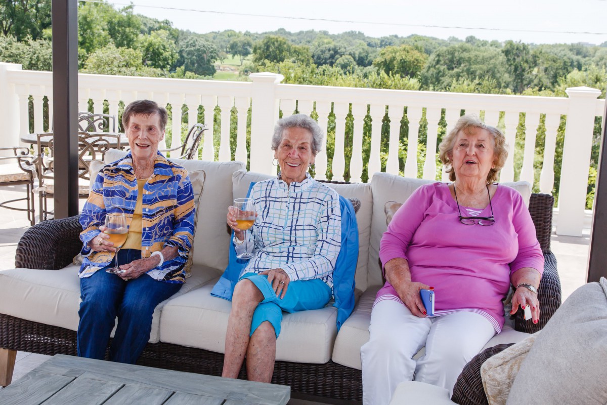 Three women enjoying a sunny day on a patio, sharing drinks and conversation.
