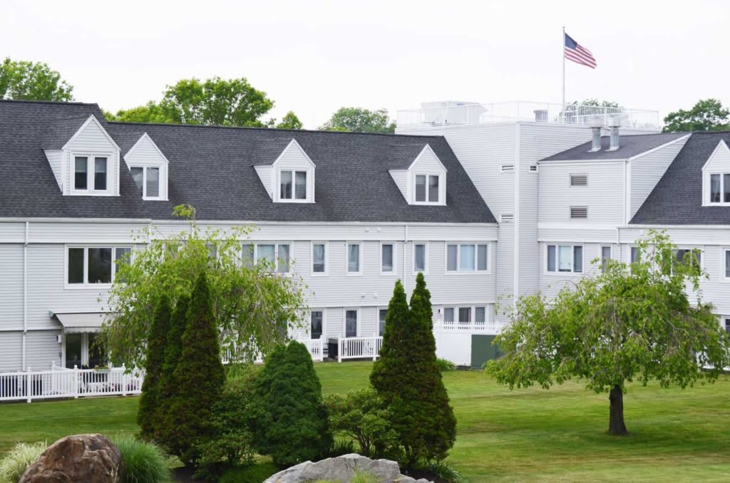 A scenic view of a large white building with an American flag, surrounded by trees and a well-maintained lawn.