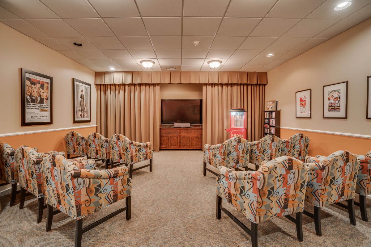 A cozy waiting room with floral chairs arranged around a television, featuring warm lighting and neutral tones.