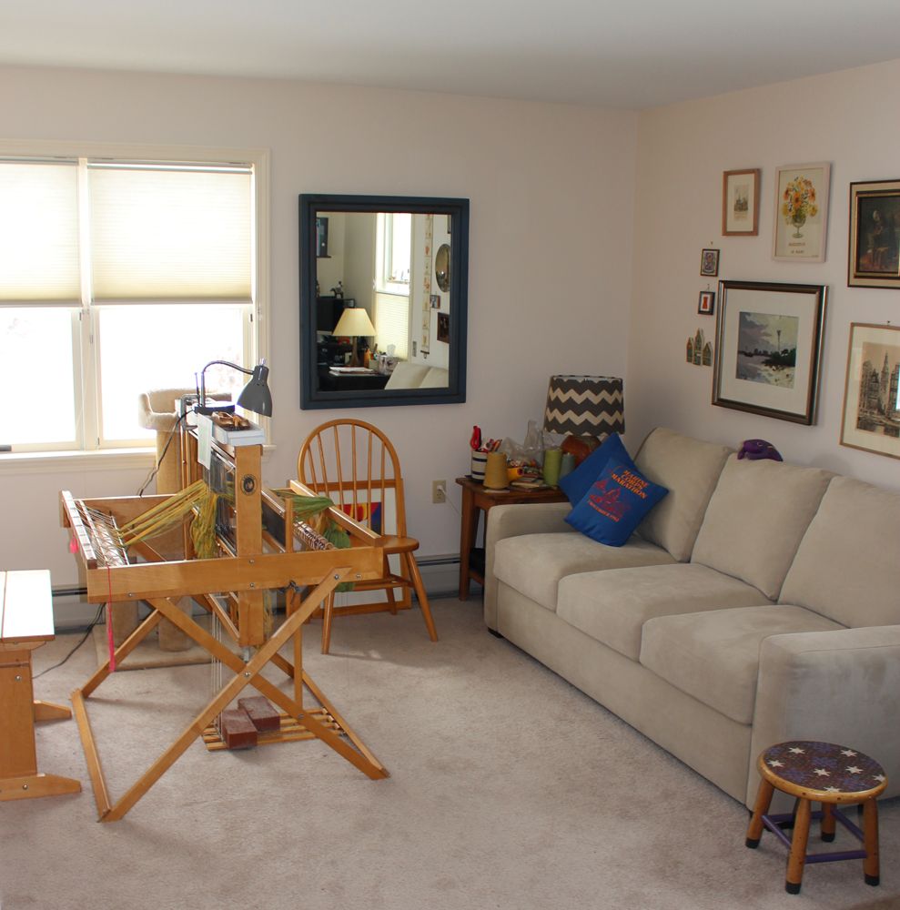 A cozy living room featuring a beige sofa, a weaving loom, and various pieces of wall art.
