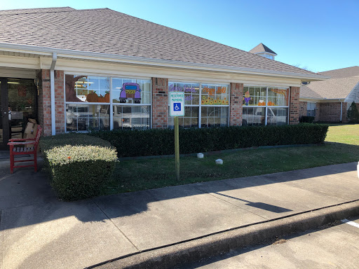 A view of a brick building with large windows, surrounded by neatly trimmed bushes.