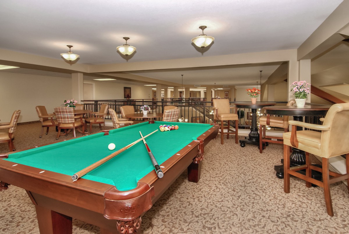 A cozy recreation area featuring a pool table surrounded by comfortable seating and warm lighting.