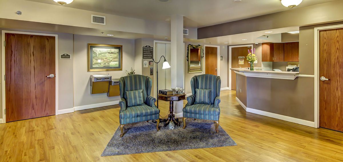 A cozy lobby area featuring two striped armchairs, a small table with a lamp, and wall artwork.