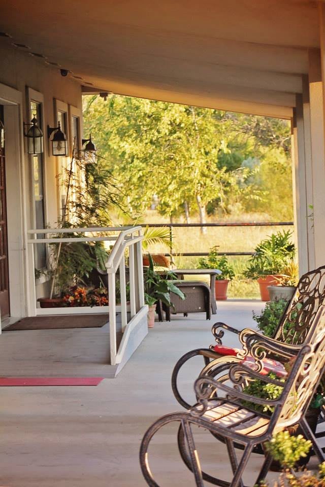 A cozy porch featuring a rocking chair and a child's bicycle, surrounded by greenery on a sunny day.
