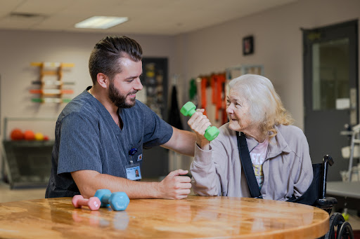 A caregiver assisting an elderly woman with her exercise routine using a dumbbell.