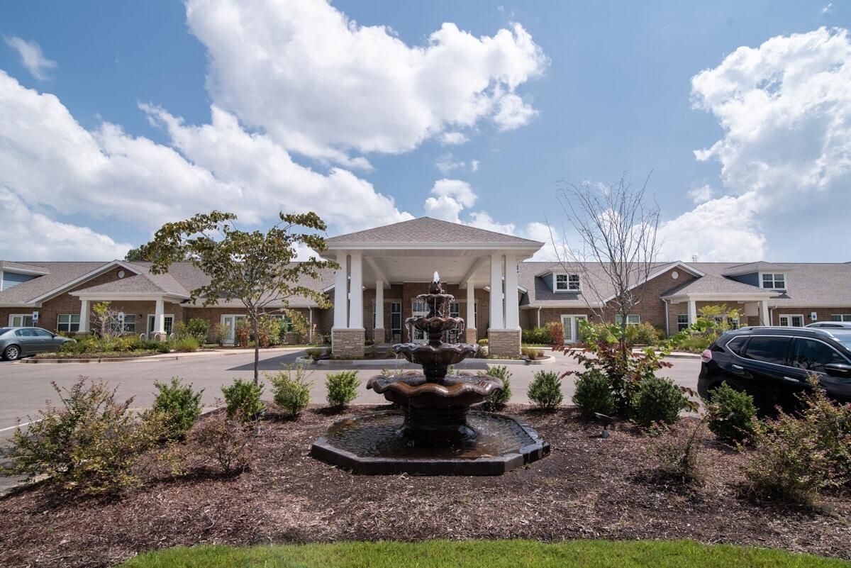 An elegant building with a landscaped entrance and a central fountain under a blue sky.