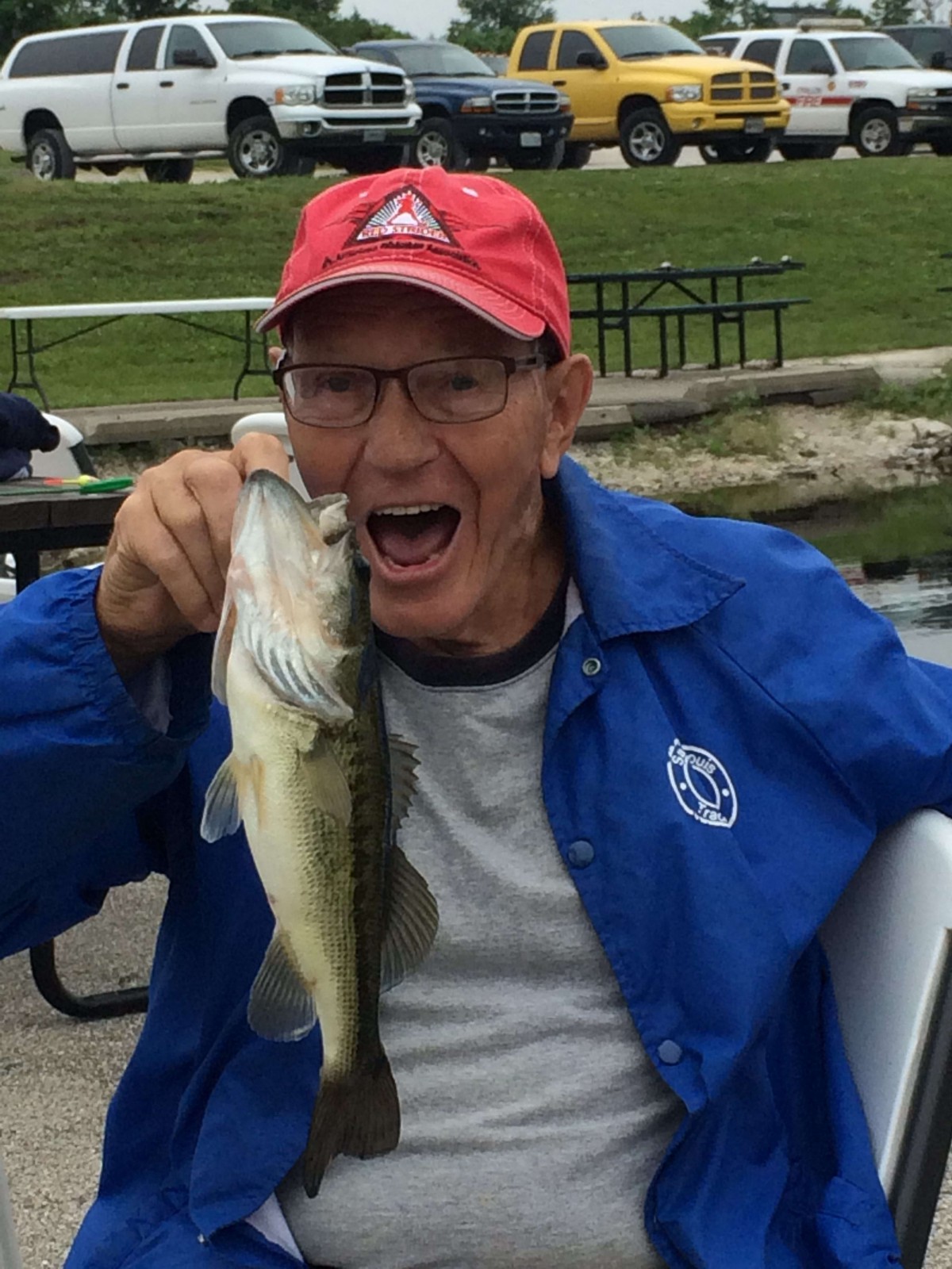 A man happily holding a fish he caught while fishing outdoors.