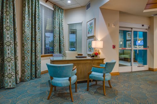 A modern office interior with a wooden desk, two turquoise chairs, and decorative elements like a lamp and artwork.