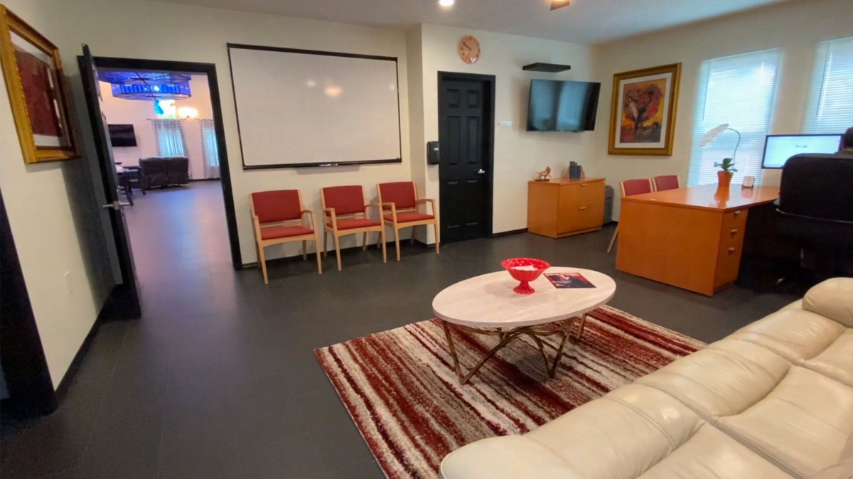 A cozy waiting room with chairs, a television, and a coffee table on a patterned rug.