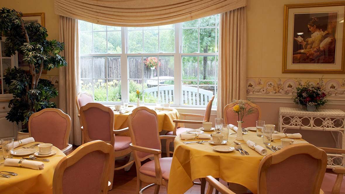 A cozy dining room with elegantly set tables near a large window offering a garden view.