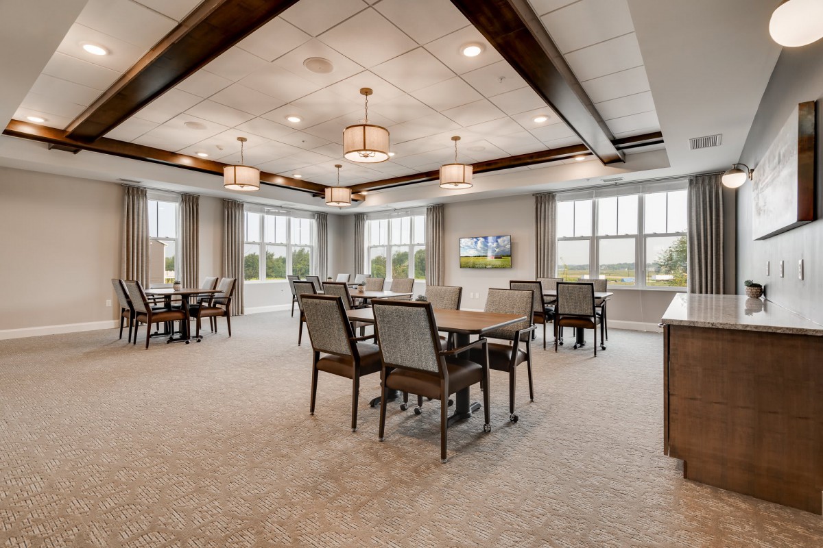 A modern dining room interior featuring tables and chairs, with ample natural light from large windows.