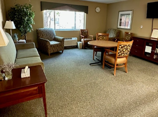 A cozy living room area featuring comfortable seating and a table, illuminated by natural light from a nearby window.