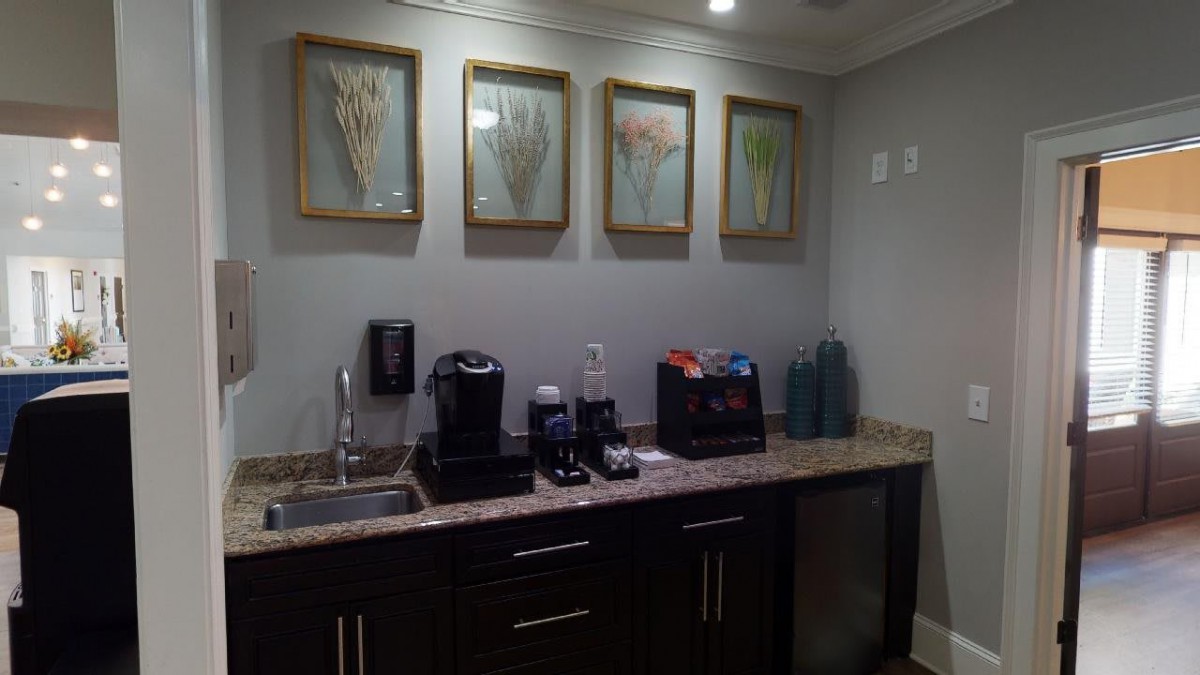 A small kitchenette area with a coffee station, including a coffee machine and various supplies, adorned with framed artwork on the wall.