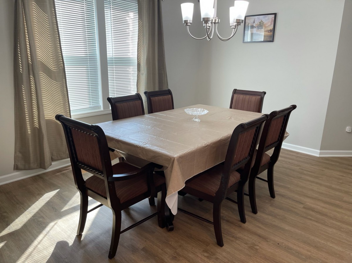 A dining room with a rectangular table and six chairs, illuminated by a chandelier.