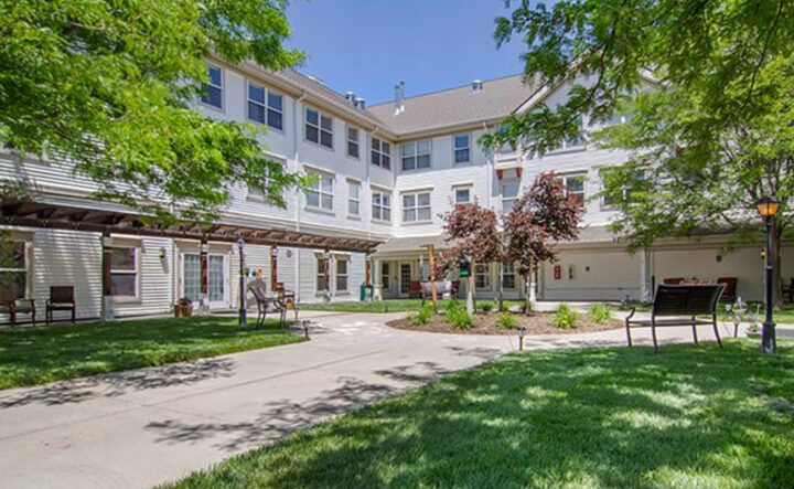 A multi-story residential building with a landscaped garden and trees in the foreground.