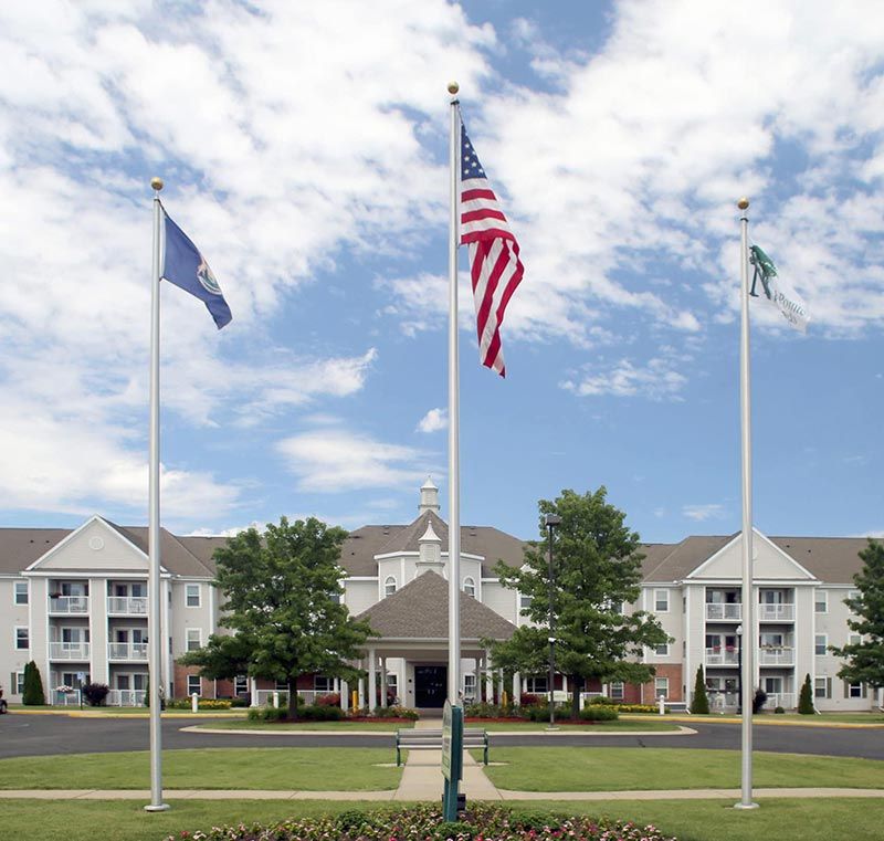 A building with flags in front, surrounded by well-maintained greenery and a partly cloudy sky.