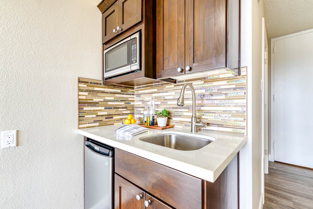 A compact kitchen area with a sink, microwave, and modern backsplash.