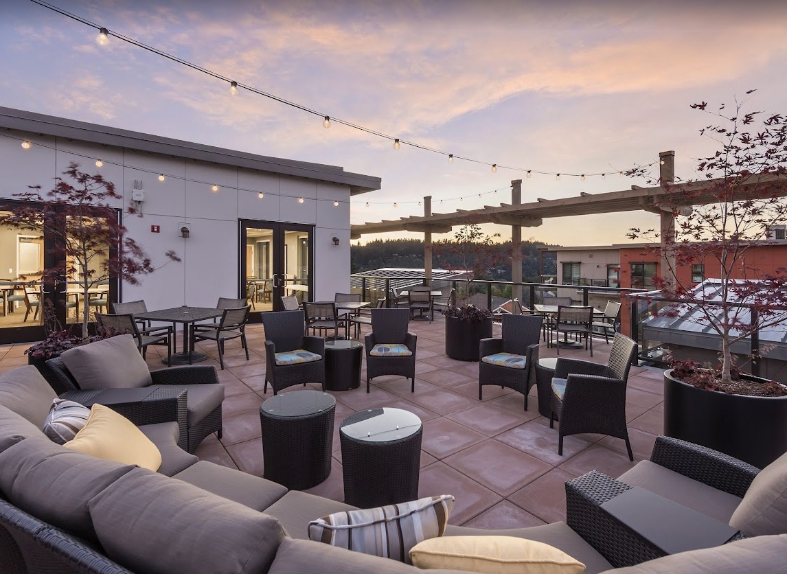 A stylish rooftop terrace with cozy outdoor seating and string lights, set against a beautiful sunset sky.