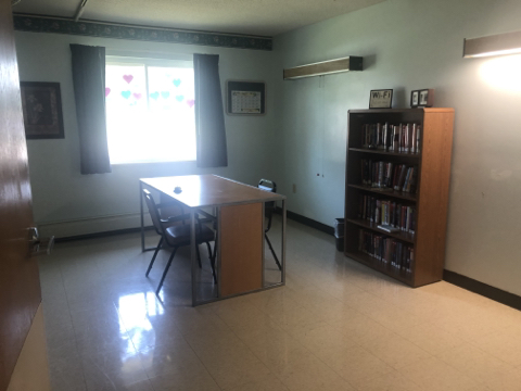 A simple, well-lit room featuring a table with chairs and a bookshelf.