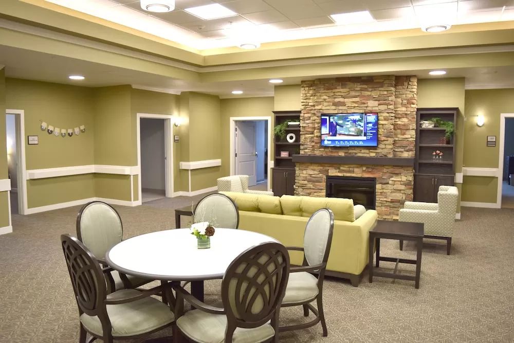 A cozy living area with comfortable seating, a mounted television above a stone fireplace, and a round table for gatherings.