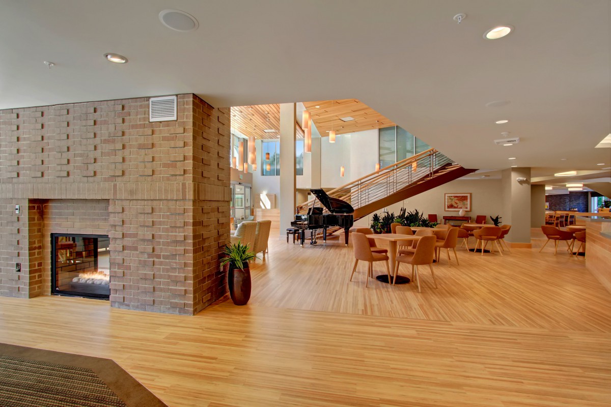 A modern interior space with wooden flooring and a grand piano, featuring ample natural light and stylish furniture.