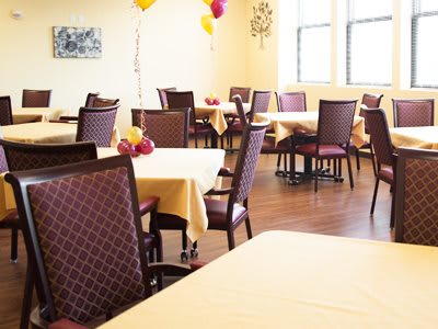 A well-lit dining area with arranged tables and chairs, decorated with balloons.